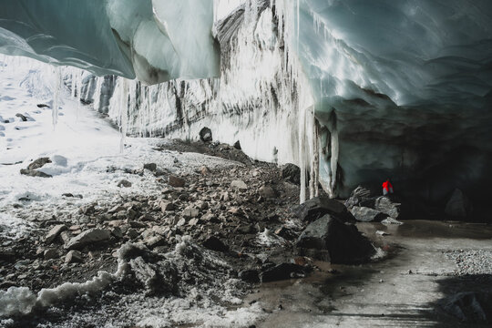 View of the Morteratsch Glacier's icy cavern, where frozen water drips and a lone figure stands at the cave's mouth, a world of cold wonder, Pontresina, Grisons Canton, Switzerland.