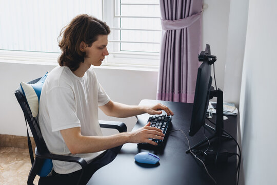 Caucasian young male working at desk with computer keyboard and mouse in home office
