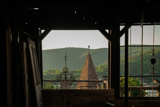 View of a historic tower's weathered stone steeple pierces the horizon beyond a rustic window frame, casting shadows in Sighisoara, Transilvania, Romania.