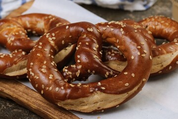 Classic pretzels topped with sesame seeds, presented on a wooden board for bakery and snack concepts.