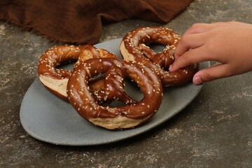 Sesame topped soft pretzels on a plate with a child hand reaching to take one, showing casual snack moment and family lifestyle concept.