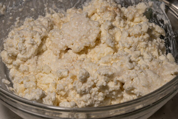 A close-up view of fresh white cottage cheese or ricotta curd with a grainy texture in a clear glass bowl.