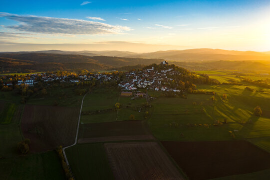 Aerial view of the village Hering with the Vetse Otzberg Castle on top of the hill, its white buildings contrasting with the dark green fields and golden sunlight, Hering, Otzberg, Hessen, Germany.