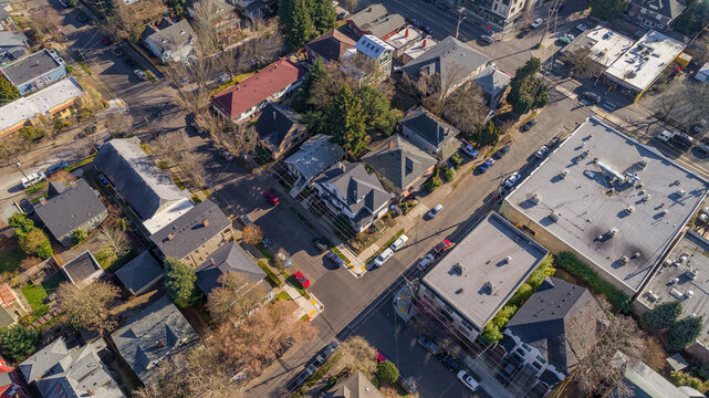 Aerial view of a quaint neighborhood intersection where Southeast 23rd Avenue meets tree-lined streets, with cars parked below the rooftops, Portland, Oregon, United States.