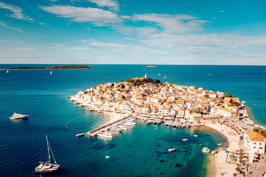 Aerial view of the old town's tight buildings contrasting with the azure sea and boats dotting the harbor, Primosten, Sibenik-Knin County, Croatia.