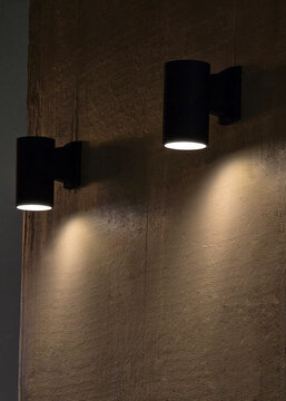 Black modern sconce lights casting warm light and shadows on an interior textured wall