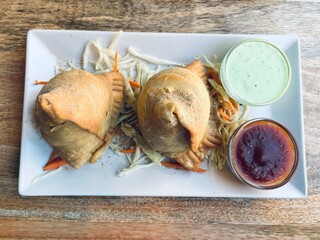 Classic Indian samosa snack with crispy dough and savory filling, plated with sauces and salad, close-up food photography.