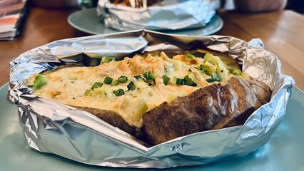 Baked potato stuffed with creamy cheese sauce, broccoli and seafood, served in foil on a plate. Comfort food concept with homemade dinner presentation.