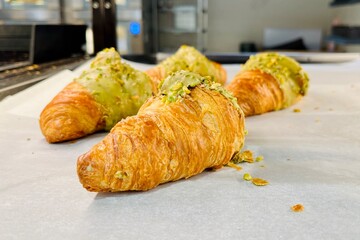 Golden croissants with pistachio filling cooling on parchment paper in a bakery workspace. Delicious homemade pastry, fresh dessert preparation and food photography background. Tasty food. Calories 