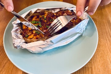 Stuffed baked potato with creamy filling, broccoli and seafood, garnished with fresh green onions. Hearty comfort food served hot in aluminum foil.
