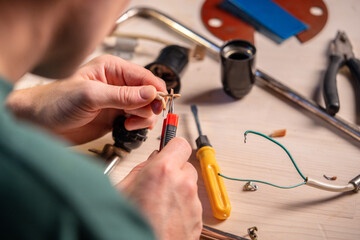 Man technician works at home workshop on repairing wiring system of vintage lamp, crafter cutting...