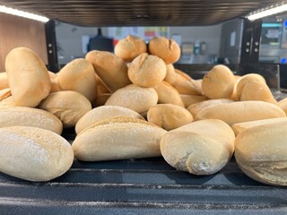 Freshly baked white bread rolls stacked on a bakery tray inside an oven. Soft round and oval buns with a light flour coating, warm golden crust, and homemade texture. Traditional baking process, artis