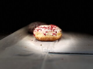 Assorted filled donuts covered with glaze and crushed dry berries on a bakery surface. Traditional sweet pastries with golden crust, creamy filling, and dramatic lighting, perfect for dessert or caf&eacute; 