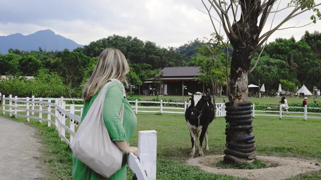 Woman walking past farm scene with mountains and animals in serene landscape