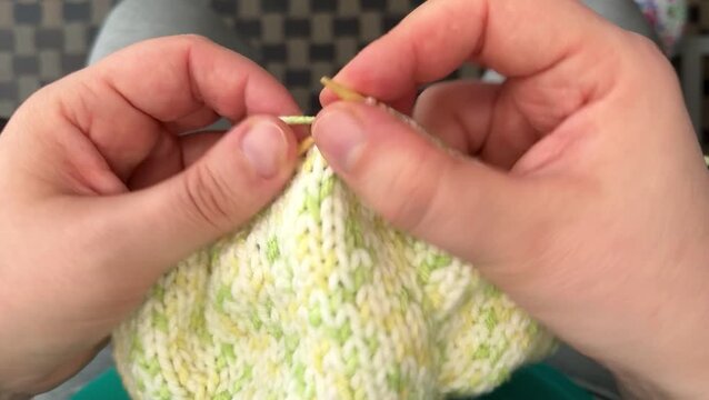 Close-up of the process of knitting a green and white dog sweater with bamboo needles using face stitches. Hobby. Handmade.