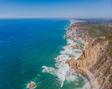 Aerial view of rugged cliffs meet the turquoise Atlantic, waves crashing against the shore in a stunning display of nature's power, Coba da Roca, Sintra, Portugal.