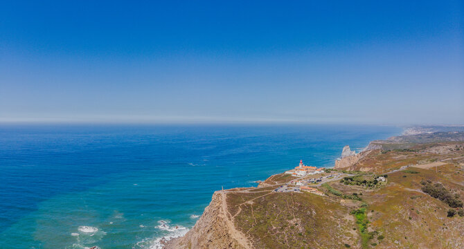 Aerial view of where the rugged cliffs meet the vast Atlantic, the lighthouse standing tall against the horizon, Coba da Roca, Sintra, Portugal.
