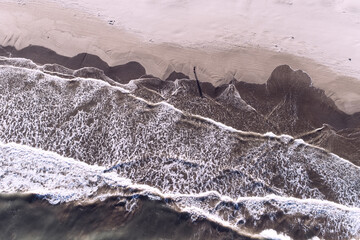 Aerial view of foamy waves crashing onto the sandy beach, where the soft beige sand meets the deep blue sea, Valencia, Valencian Community, Spain.