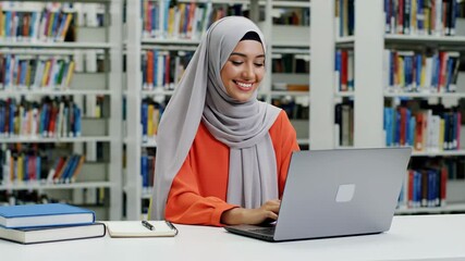 Young female student wearing hijab working on laptop in library