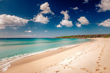 View of sandy beach meeting turquoise water under a bright sky dotted with fluffy clouds, footprints marking the shore in Taipei City, Taiwan.