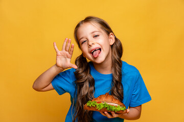 Happy little girl eating a croissant, sandwich. Unhealthy fast food, proper nutrition concept....