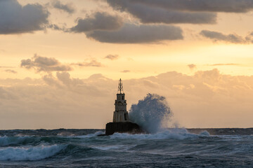 View of a lighthouse battered by crashing waves under a dramatic, golden sky, a beacon of resilience against the turbulent sea, Ahtopol, Ahtopol, Bulgaria.