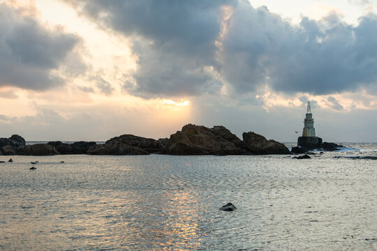 View of the Ahtopol Lighthouse standing tall against the sunset sky, waves gently lapping against the rocky shore, Ahtopol Lighthouse, Ahtopol, Bulgaria.