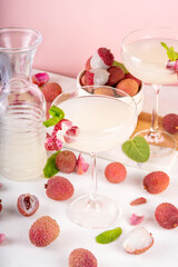 Lychee fruit tasty martini cocktail. Tasty alcohol drink with fresh lychees, mint leaves, liqueur and sweet sour juice, on white pink table background with ripe raw lychee fruits, copy space