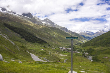 Aerial view of winding roads snaking through lush green valleys, contrasting with the rugged, snow-capped peaks of the Swiss Alps, Obergoms, Valais, Switzerland.