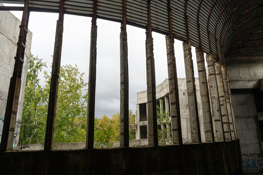 View of crumbling concrete pillars frame a vista of verdant trees and skeletal building remains against a grey sky, Perla 2, Primorsko, Bulgaria.