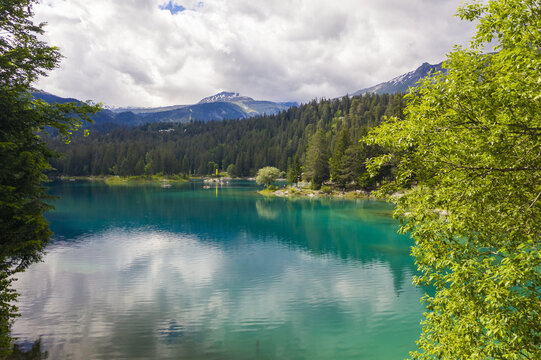 Aerial view of the shimmering turquoise waters of Lake Cauma reflecting the sky and surrounding forests, a serene alpine vista, Flims, Grisons, Switzerland.