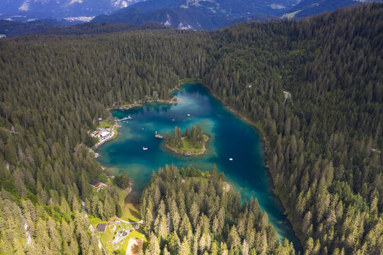 Aerial view of the vibrant turquoise waters of Lake Cauma nestled amidst a dense forest, a serene island at its heart, Flims, Grisons, Switzerland.