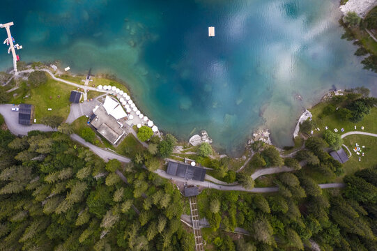 Aerial view of the shimmering turquoise waters meet the lush green shoreline lake Cauma dotted with buildings and pathways, a serene alpine escape., Flims, Grisons, Switzerland.