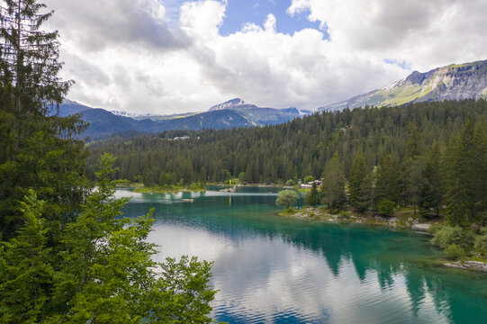 Aerial view of the turquoise lake Cauma mirroring the sky, embraced by the lush forest and imposing mountains, a serene vista of nature's artistry, Flims, Grisons, Switzerland.