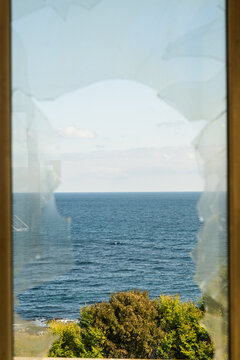 View of the sea through a cracked window, the blue water contrasts with the light sky and green bushes, Costa del croco, Tsarevo, Bulgaria.