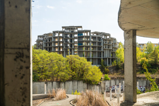 View of an unfinished concrete building rises amidst lush greenery and decaying structures, a stark contrast of construction and abandonment, Costa del croco, Tsarevo, Bulgaria.