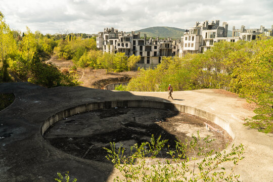 View of a solitary figure walks along the edge of a concrete structure, amidst the skeletal remains of abandoned buildings, Costa del croco, Tsarevo, Bulgaria.