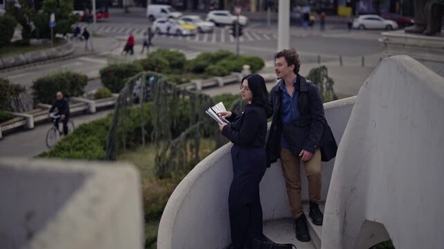 Two focused business people observe a busy city intersection, engaged in conversation while reviewing documents. They then proceed to walk down, ready for their next task.