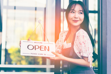 Female owner of coffee shop or restaurant turning round sign to open. Smiling young asian woman owner, employee retail coffee shop woman hand in setting sign board to open for welcome customer, reopen
