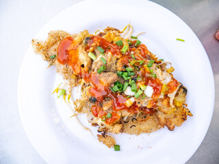 Crispy Thai Oyster Omelette (Hoi Tod) topped with sweet chili sauce and fresh spring onions on a white plate