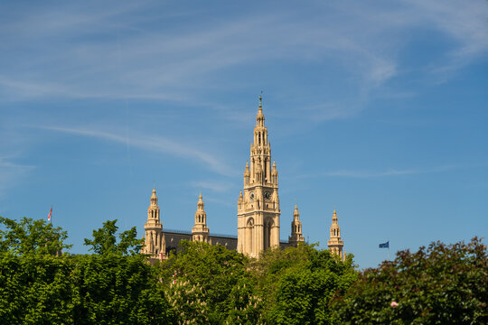 View of the Rathaus's gothic spire piercing the bright blue sky, framed by verdant trees in full leaf, a blend of nature and architecture, Vienna, Vienna, Austria.