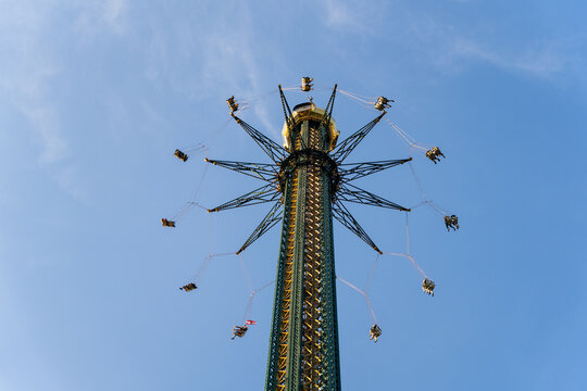 View of riders twirling high on a chain swing ride against the stark blue sky, creating a dizzying, thrilling spectacle, Vienna, Vienna, Austria.