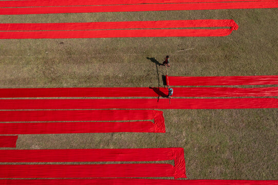 Aerial view of vibrant red cloths stretched across the green field, creating a striking contrast under the sun, Narsingdi, Dhaka Division, Bangladesh.
