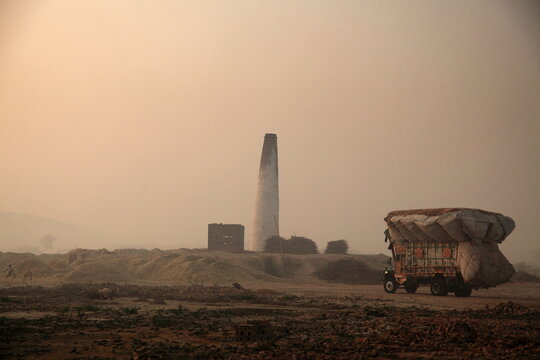 View of a truck heavily laden with goods passes a towering brick kiln under a hazy sky, creating a scene of industry and transport, Mithi, Sindh, Pakistan.