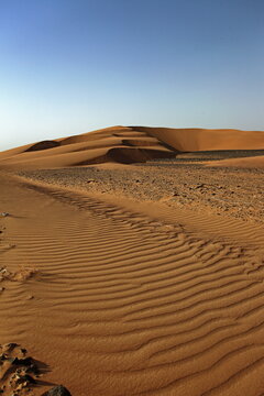 View of undulating golden sand dunes stretching towards the horizon under a clear sky, marked by subtle textures and shadows, Noshki, Balochistan, Pakistan.