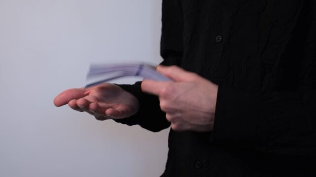 Young man in black shirt handling a stack of banknotes in his hands on white background close-up of hands