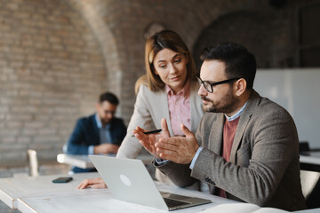  Professional manager showing data on a laptop to his colleagues in a modern office.