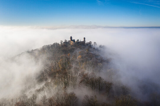Aerial view of imposing Schloss Auerbach castle silhouette piercing through a sea of ethereal fog, perched atop a forested hill, creating a dreamy landscape, Bensheim, Hessen, Germany.