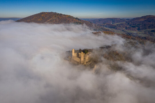 Aerial view of Schloss Auerbach castle shrouded in the ethereal embrace of dense clouds, with golden sunlight kissing the mountaintop, Bensheim, Hessen, Germany.