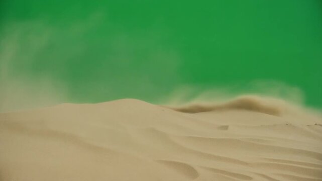 A low-angle close-up shot of desert sand dunes with a dust storm blowing across a bright green screen background